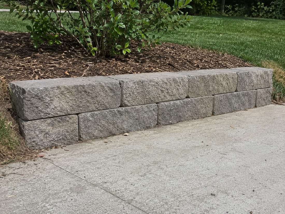 Interlocking grey block retaining wall along a driveway